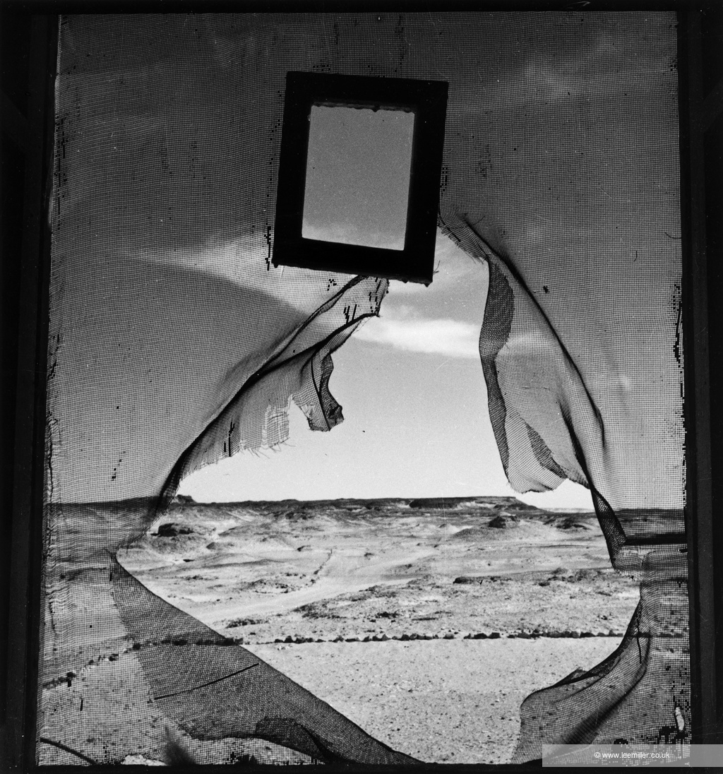 Lee Miller photograph looking through ripped side of tent or mesh at desert landscape beyond