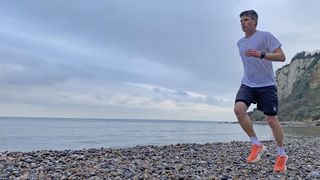 Man running in Adidas Terrex Agravic Speed Ultra running shoes (and adidas Terrex socks, and adidas Terrex T-shirt) on a pebbly beach