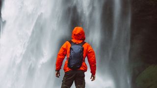 best dry bag: a man wearing a dry bag standing in front of a waterfall