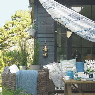 outdoor living area with printed sail shade, outdoor sofa and armchair, lighting, coffee table, nautical theme