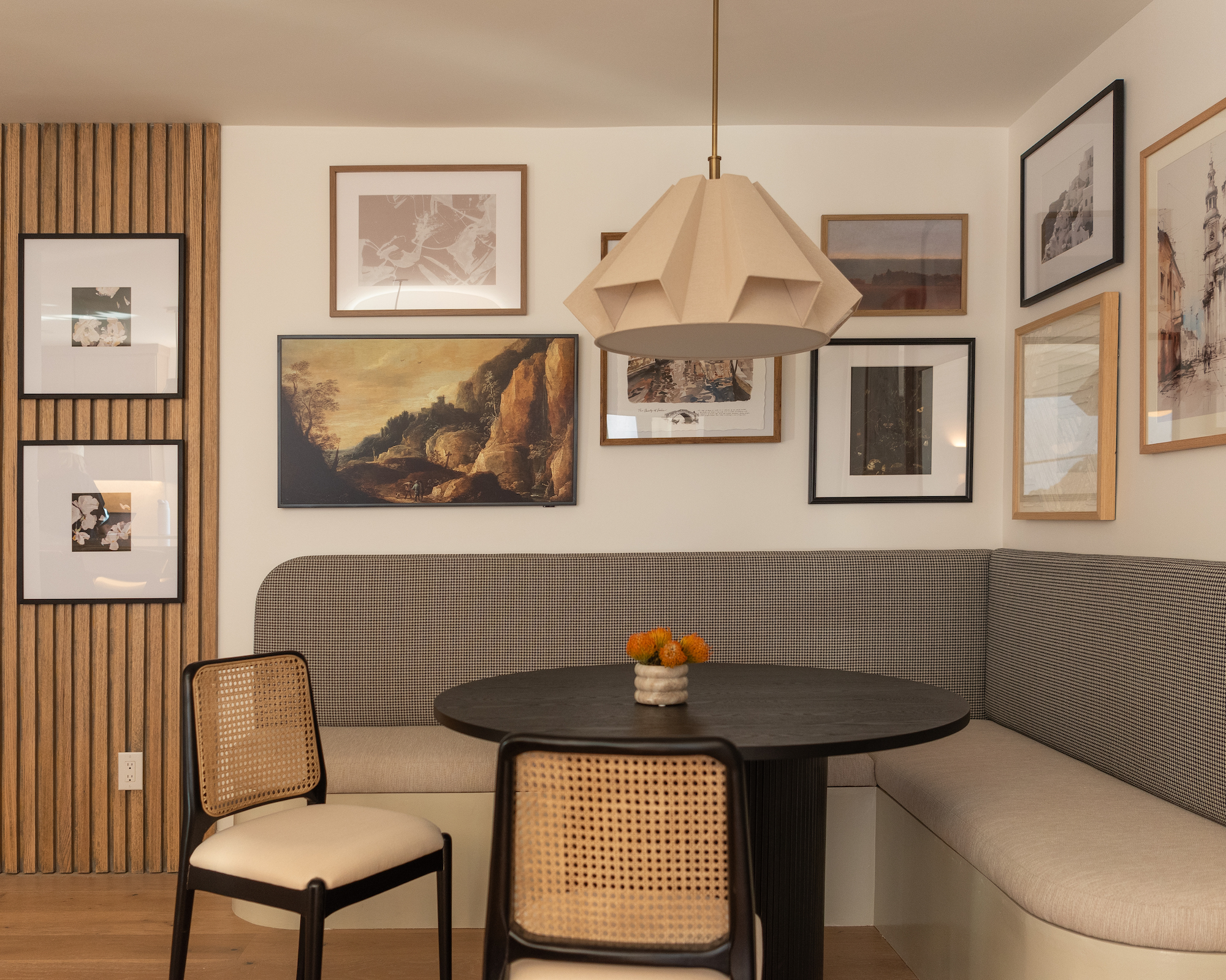 Breakfast nook with banquette upholstered in neutral shades, pendant light, art on wall and light wood paneling