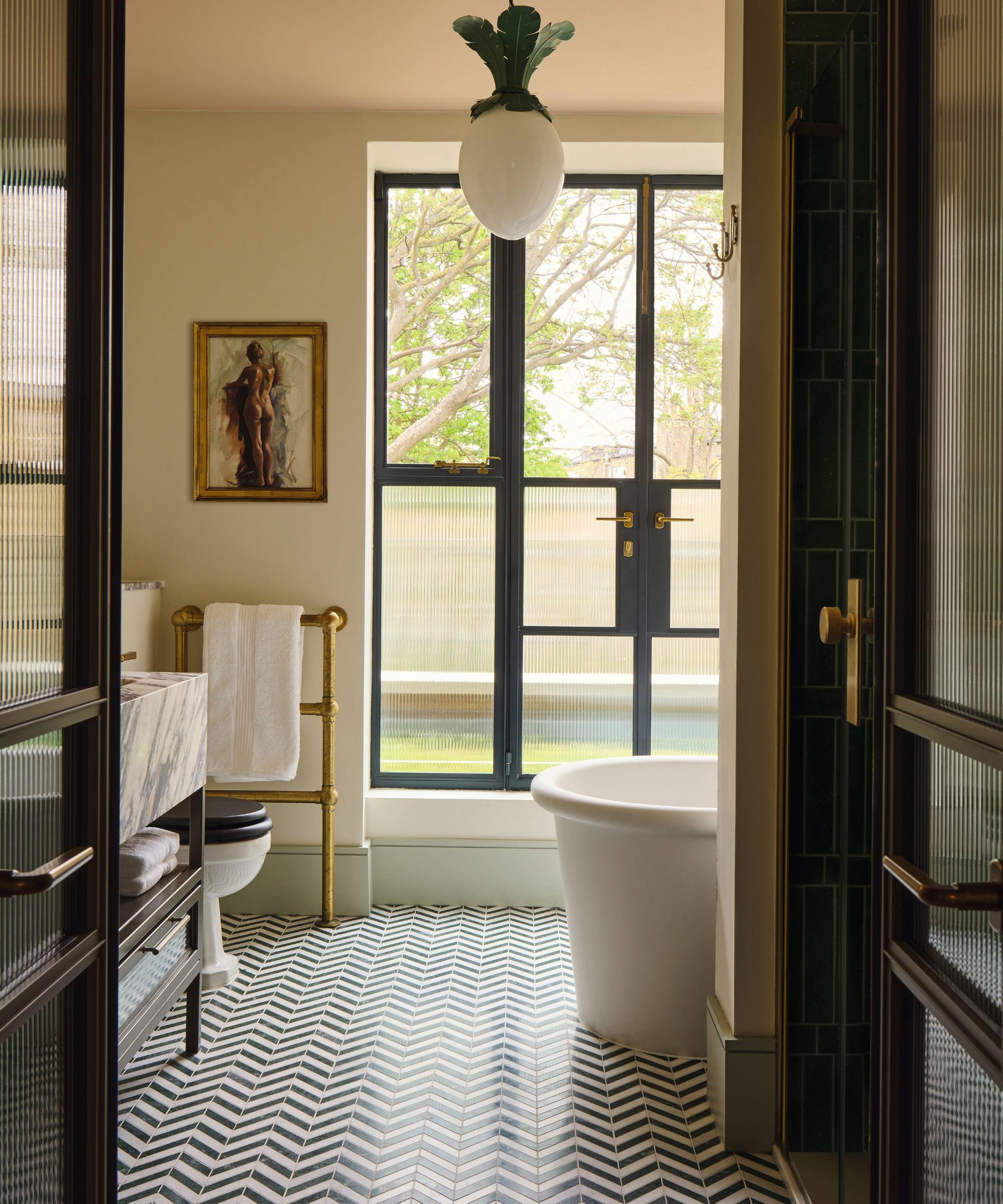 a soft primary bathroom with freestanding tub, herringbone black and white tiled floor, brass fixtures, crittal doors to the balcony and a Beata Heuman egg lamp