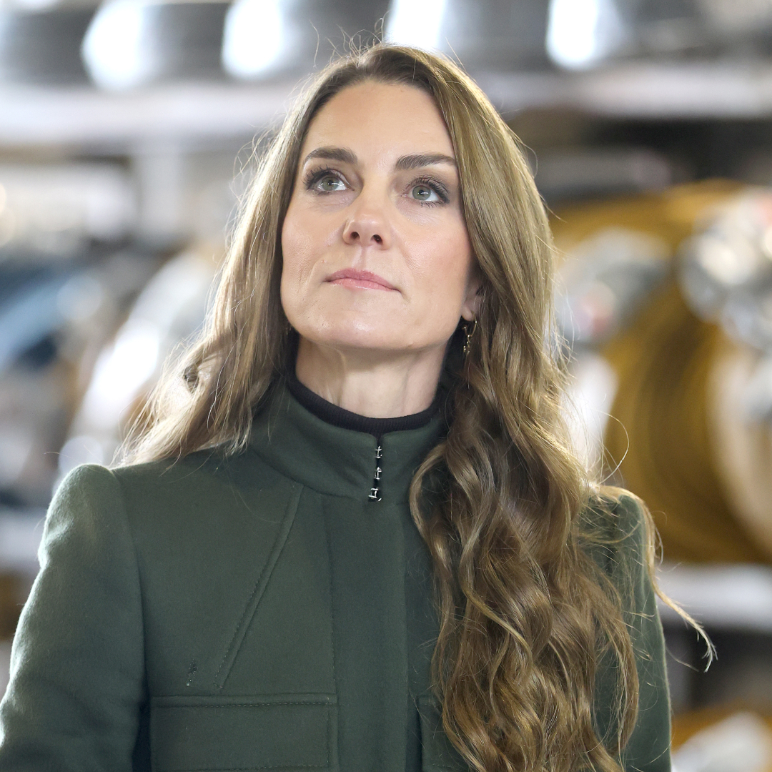 Princess Kate Middleton has long brown wavy hair with blonde highlights and looks to the sky while wearing a dark green coat