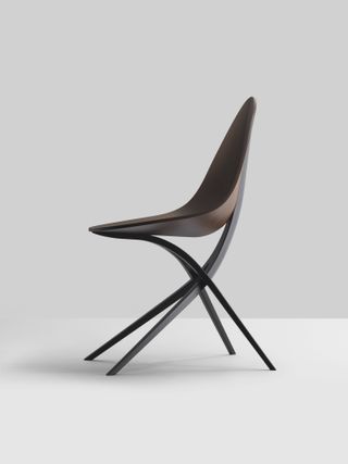 The dark brown chair has four legs that cross each other on either side with the front and back legs supporting the opposite part of the chair. The base is one curved piece at an angle on someone sitting.