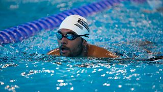 Man wearing white swimming cap and goggles swims in indoor pool