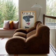 A living room with large windows, a curved floor lamp and a brown velvet sofa