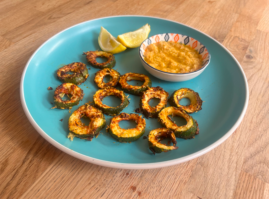 Crisped rings of zucchini, a dip in a small blue and lemon wedges on a blue plate on a wooden table