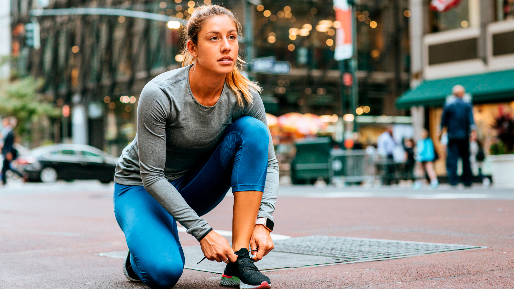 Woman on one knee tying a running she. A city street is in the background