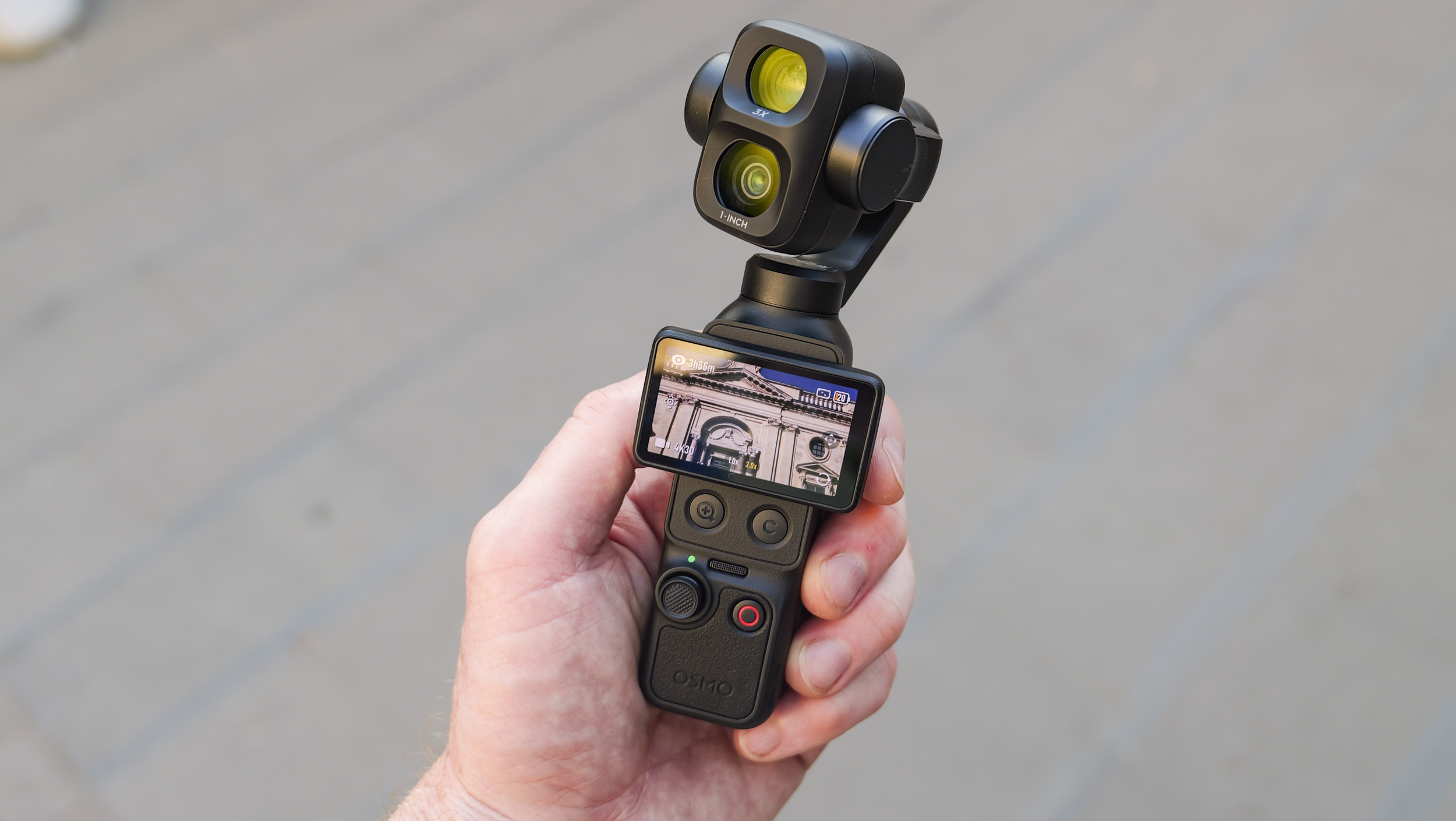 DJI Osmo Pocket 4P vlogging camera in a person's hand in a city street, screen rotated horizontal