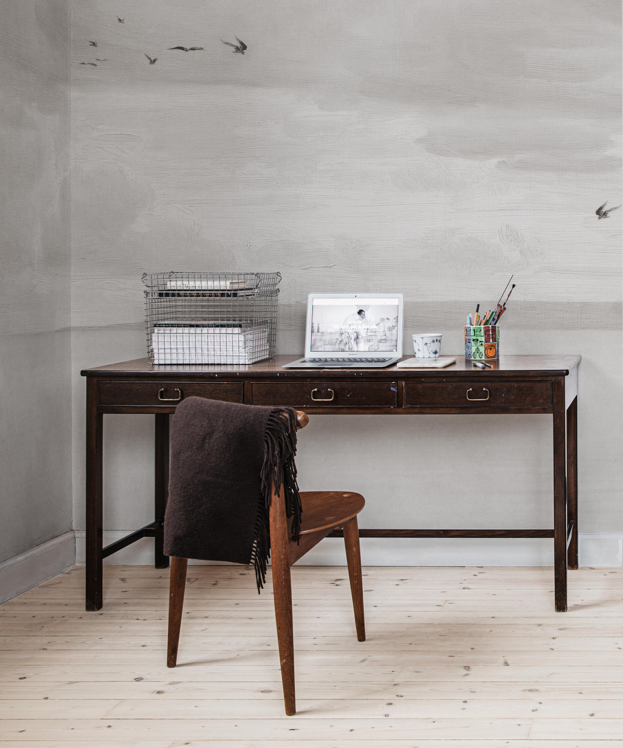 desk and chair in space decorated with grey wallpaper showing clouds and flying birds