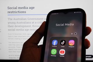 A mobile phone showing social media apps in front of a screen stipulating Australia's social media age restrictions