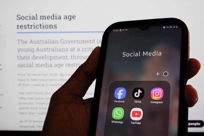 A mobile phone showing social media apps in front of a screen stipulating Australia&#039;s social media age restrictions