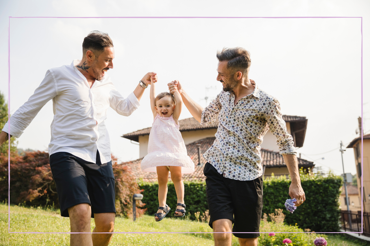 Happy gay couple playing with their child in the garden