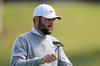 Scottie Scheffler hands his caddie his putter