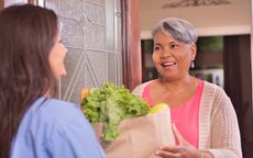 A woman accepts a bag of groceries delivered to her front door