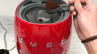 Adding a scoop of coffee to the smeg drip coffee maker filter basket