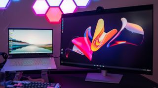 Bästa välvda datorskärm i 4K: En Dell UltraSharp U3223QZ står bredvid en laptop på ett skrivbord, med en färgglad bakgrundsbild som matchar NanoLeaf-panelerna på väggen i bakgrunden.