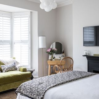 A white bedroom with an olive green sofa in the bay window