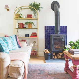 White living room with a log burner in the middle, a gold shelving rack to the side and a cream sofa in the room