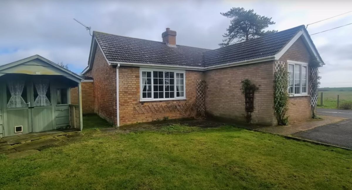 A bungalow with green shed housing a septic tank that is falling down next to it