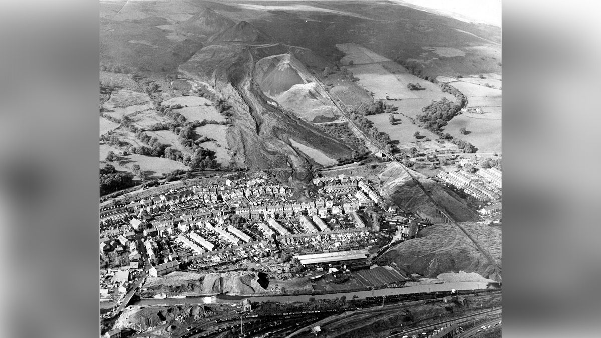 Aerial shot of coal tip that has slid down hillside engulfing houses and a school in town below.