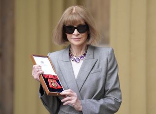 Anna Wintour wearing a gray blazer and black sunglasses holding a box with a Companion of Honour award standing outside at Buckingham Palace