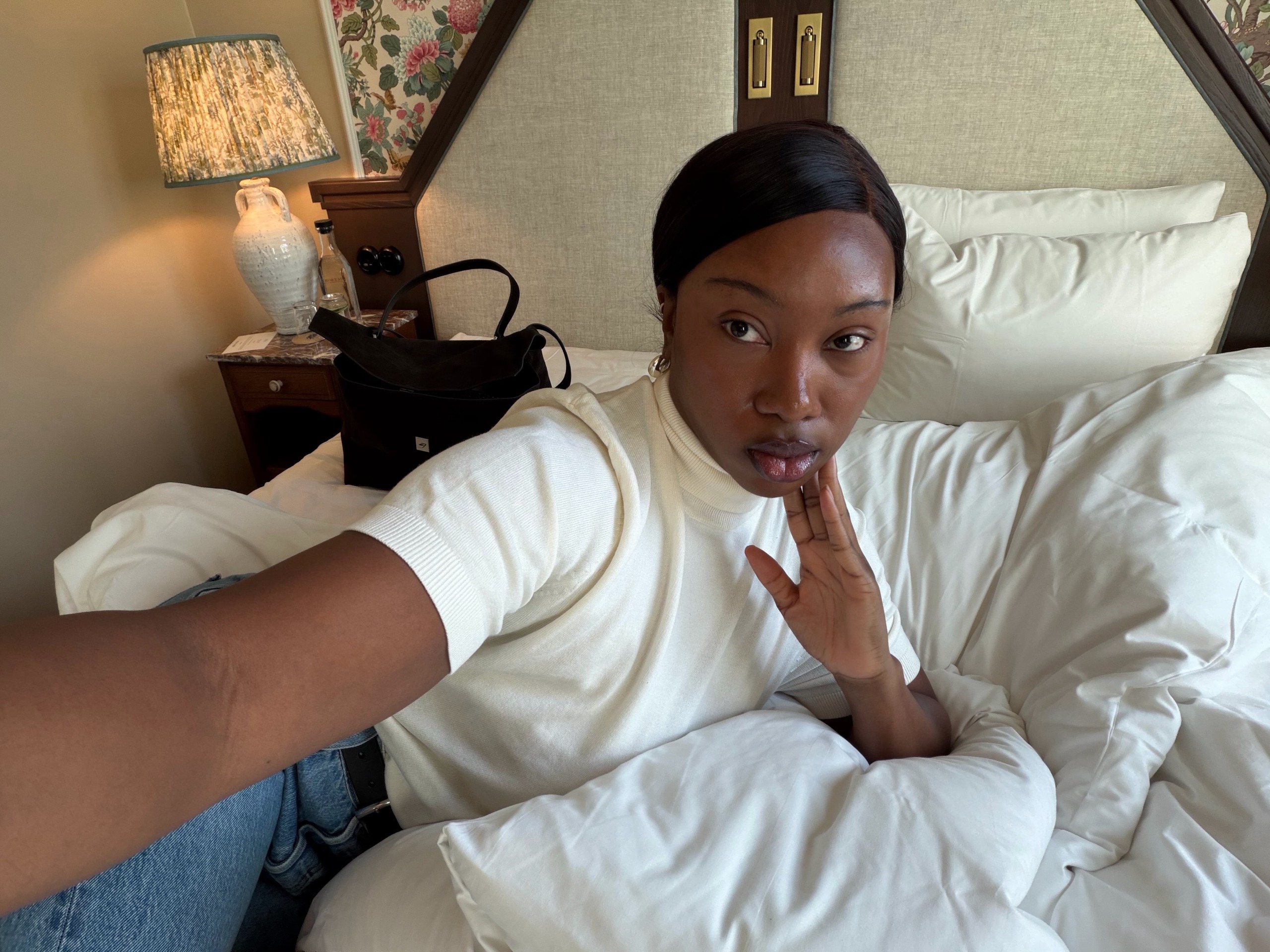 A woman taking a selfie from bed in a white T-shirt and jeans.