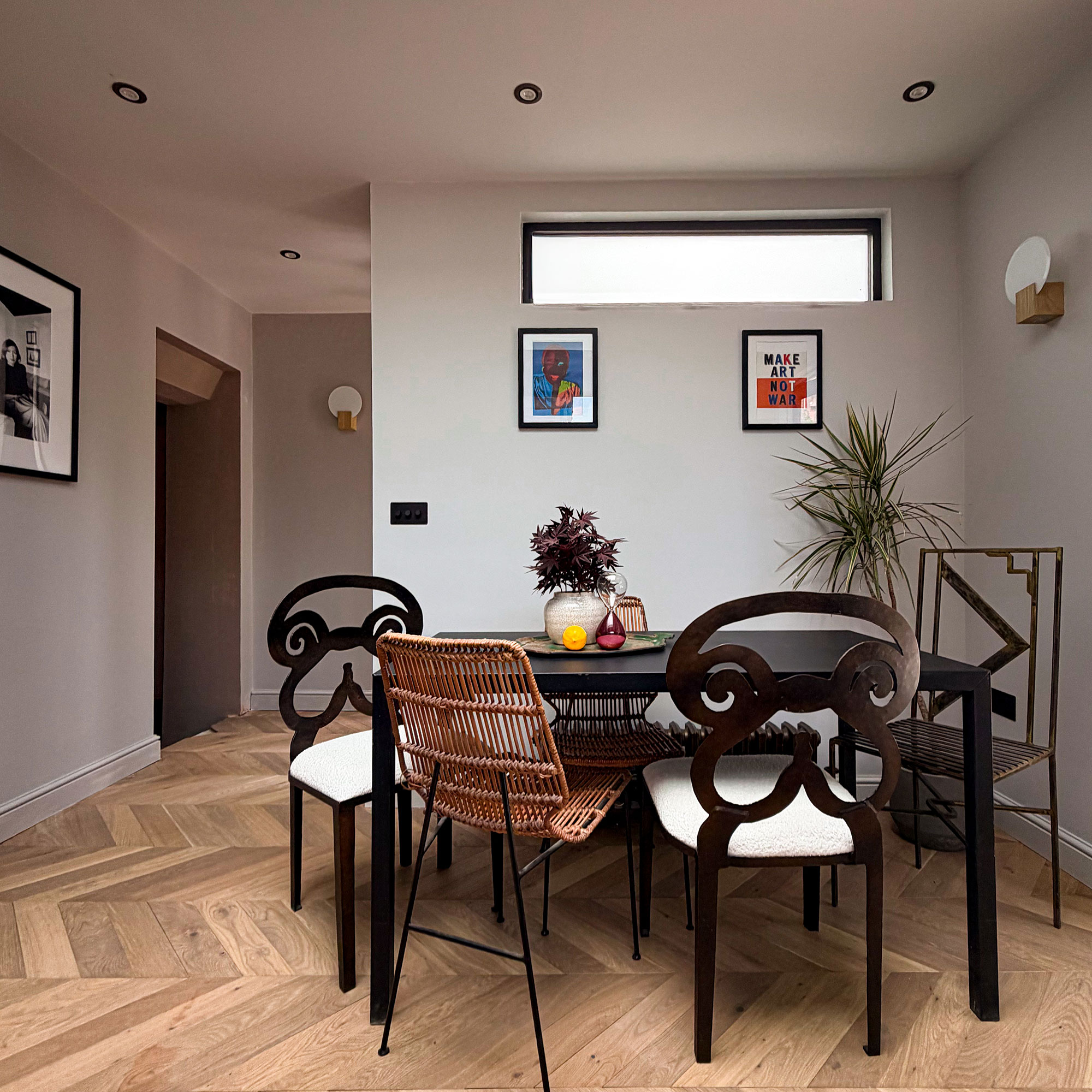 Kitchen dining area with grey walls, wooden chevron flooring, spotlights and five mismatched chairs around dark wood table