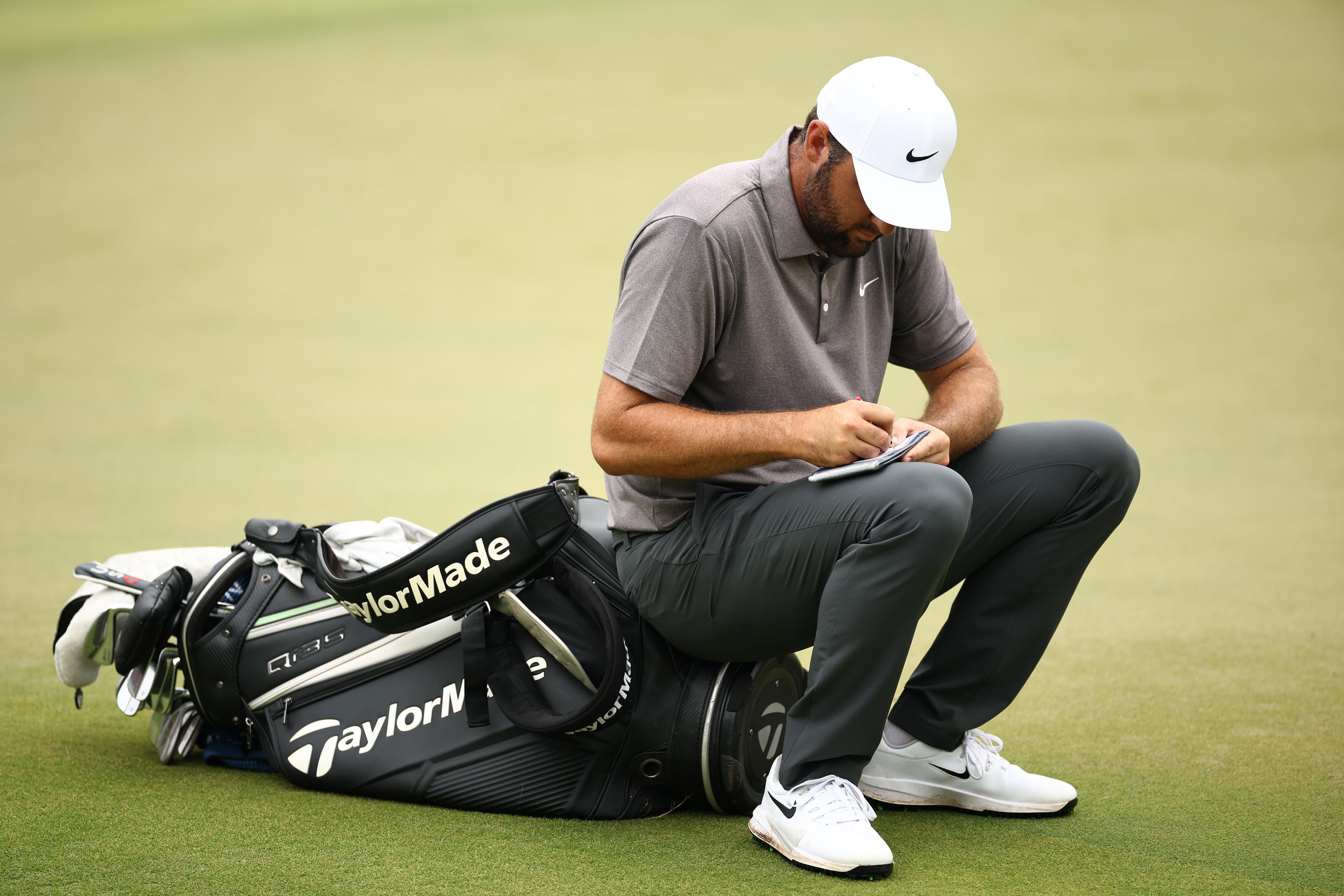 Scottie Scheffler sitting on his tour bag writing his score