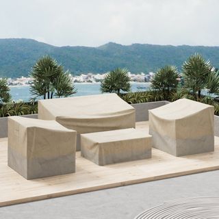 4-Piece cream Outdoor Patio Furniture Covers, in place on a light wooden deck overlooking a bay with mountain backdrop