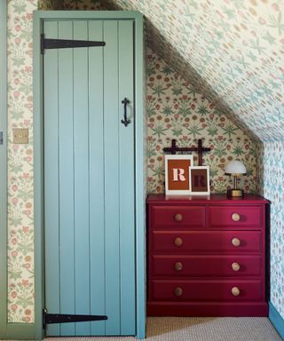 small wardrobe built under sloping ceiling and painted to match floral wallpaper