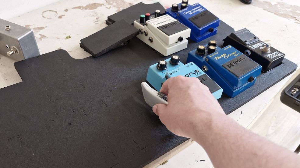 A man cuts the pedal tray foam of a Boss BCB-90X pedalboard