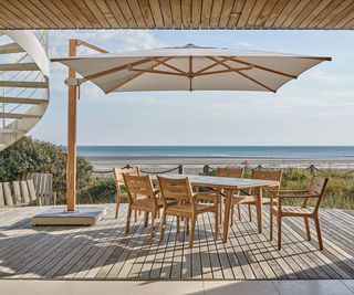 teak outdoor dining table and chairs underneath a patio umbrella on a covered patio
