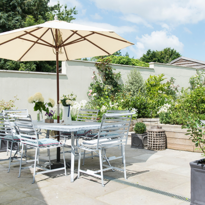 Garden dining table and chairs complete with white parasol on a garden patio, surrounded by greenery in pots and planters.