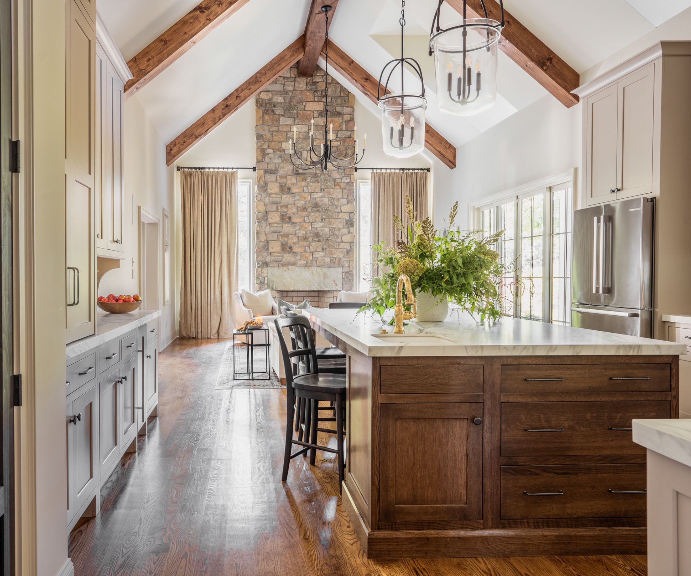 An open plan kitchen and living area with vaulted ceilings, white cabinets, and a wooden island filled with a mix of drawers and cabinet storage