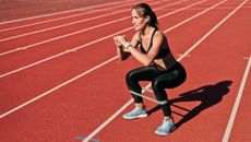Woman wearing sportswear on running track squats with a resistance band around her calves