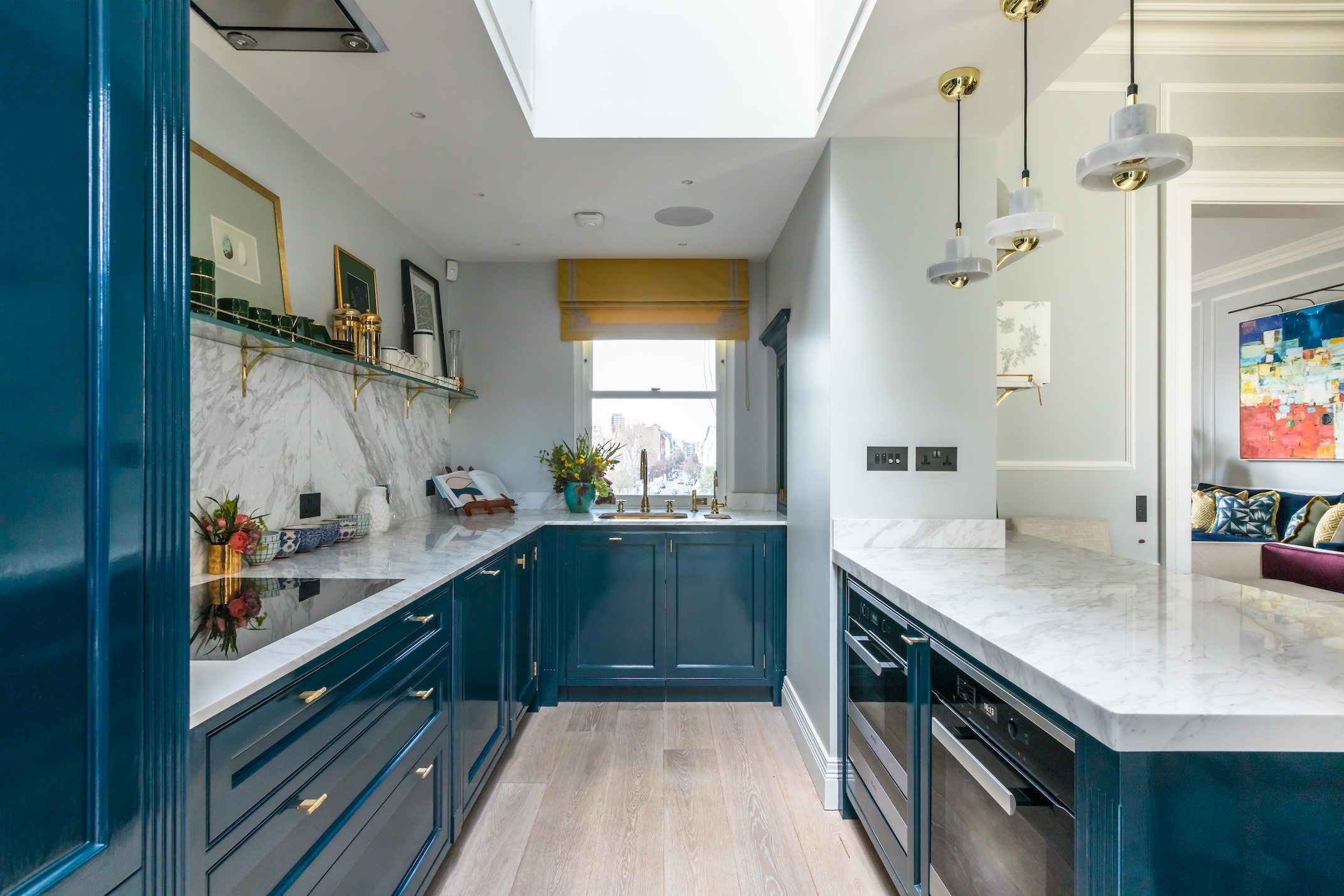 A long narrow blue kitchen with open shelving down one side, a window at the end and a peninsula on the other