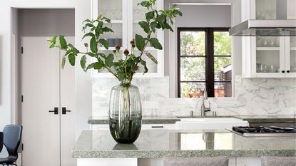 A white kitchen with granite countertops, and a lage glass vase of flowers on the island
