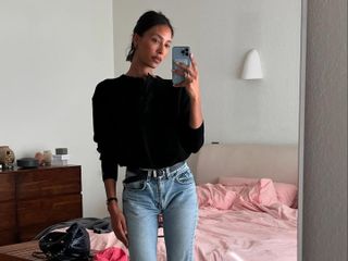 L.A. woman takes a mirror selfie in a The Row sweater, vintage skinny jeans, a black belt and black flats.