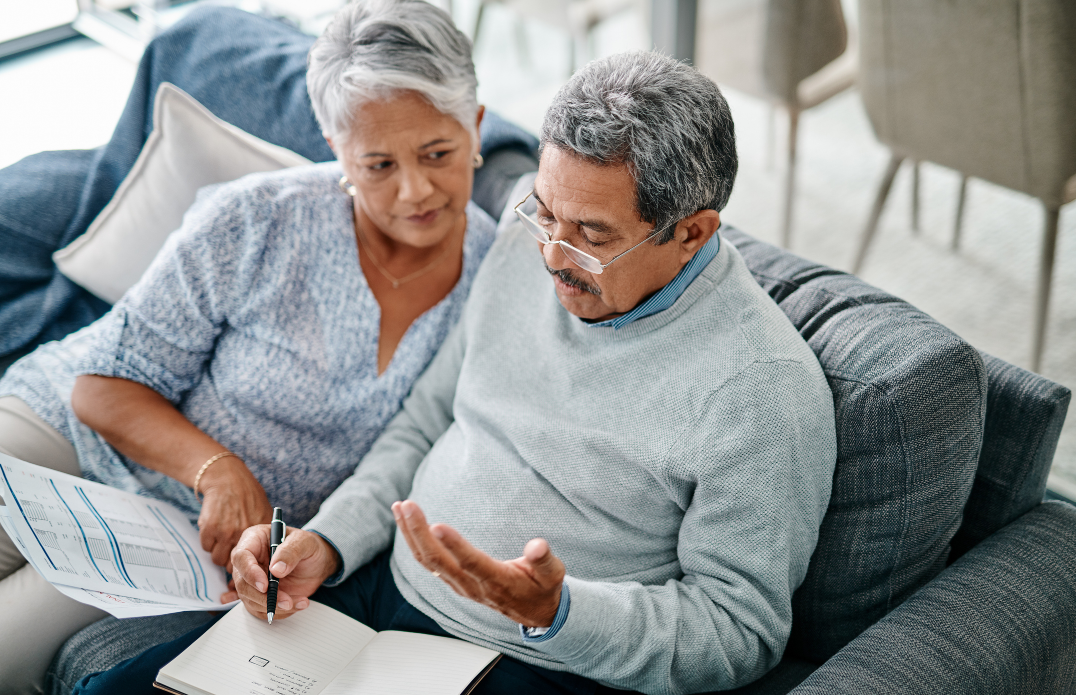 A senior couple discusses their finances while sitting on the couch.