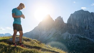 Young man trail running on the mountain, looking a sport watch