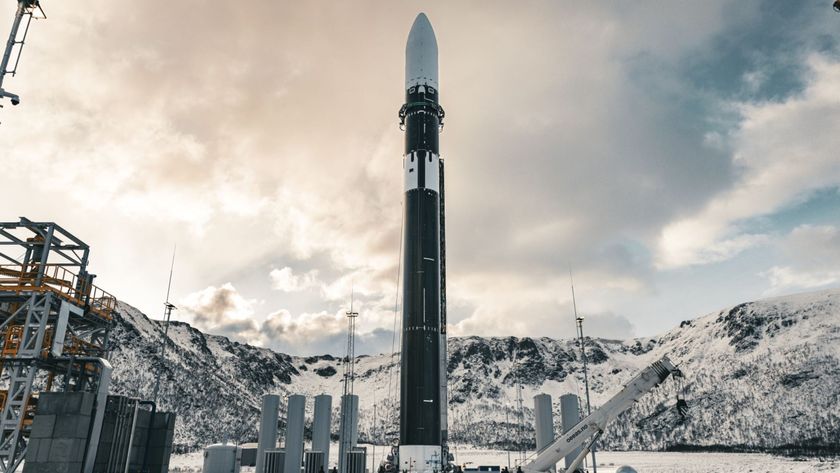 a white-tipped black rocket stands against a backdrop of snowy hills and a cloudy bright sky.