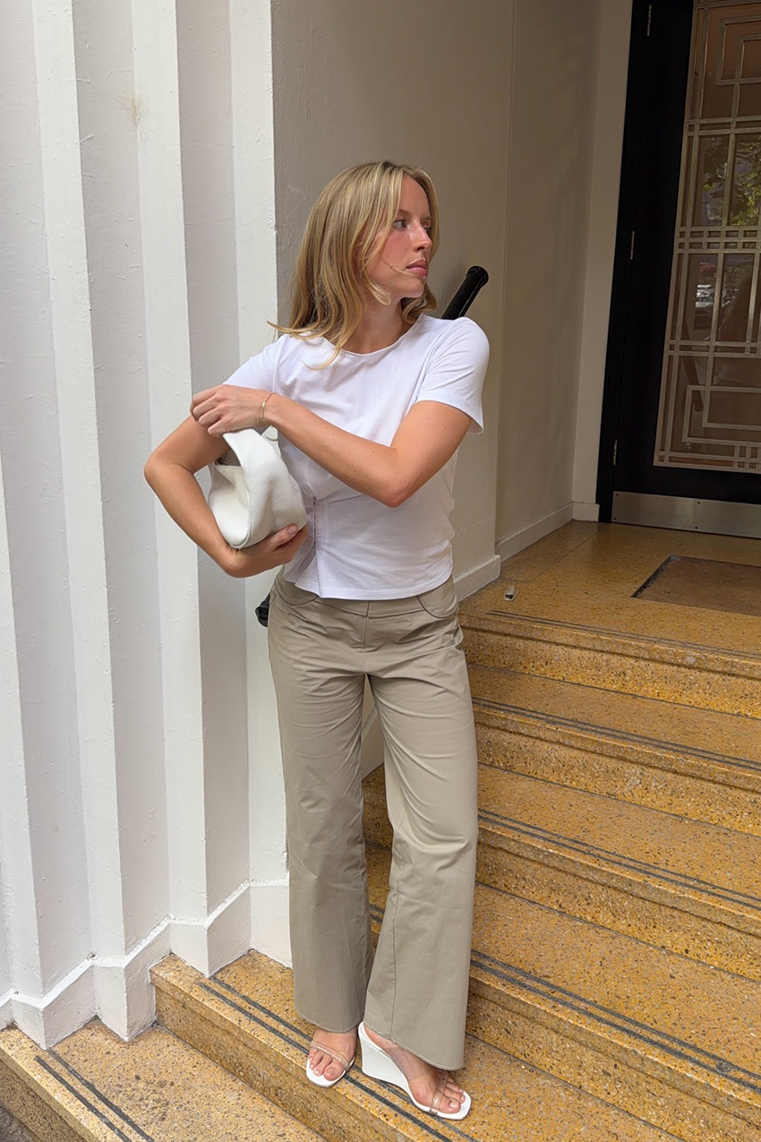 A woman wearing a white tee, khaki pants, white wedge sandals and a white shoulder bag.