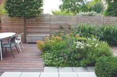 Patio planting ideas in a decked garden with slatted wooden fence and modern white table and chairs.
