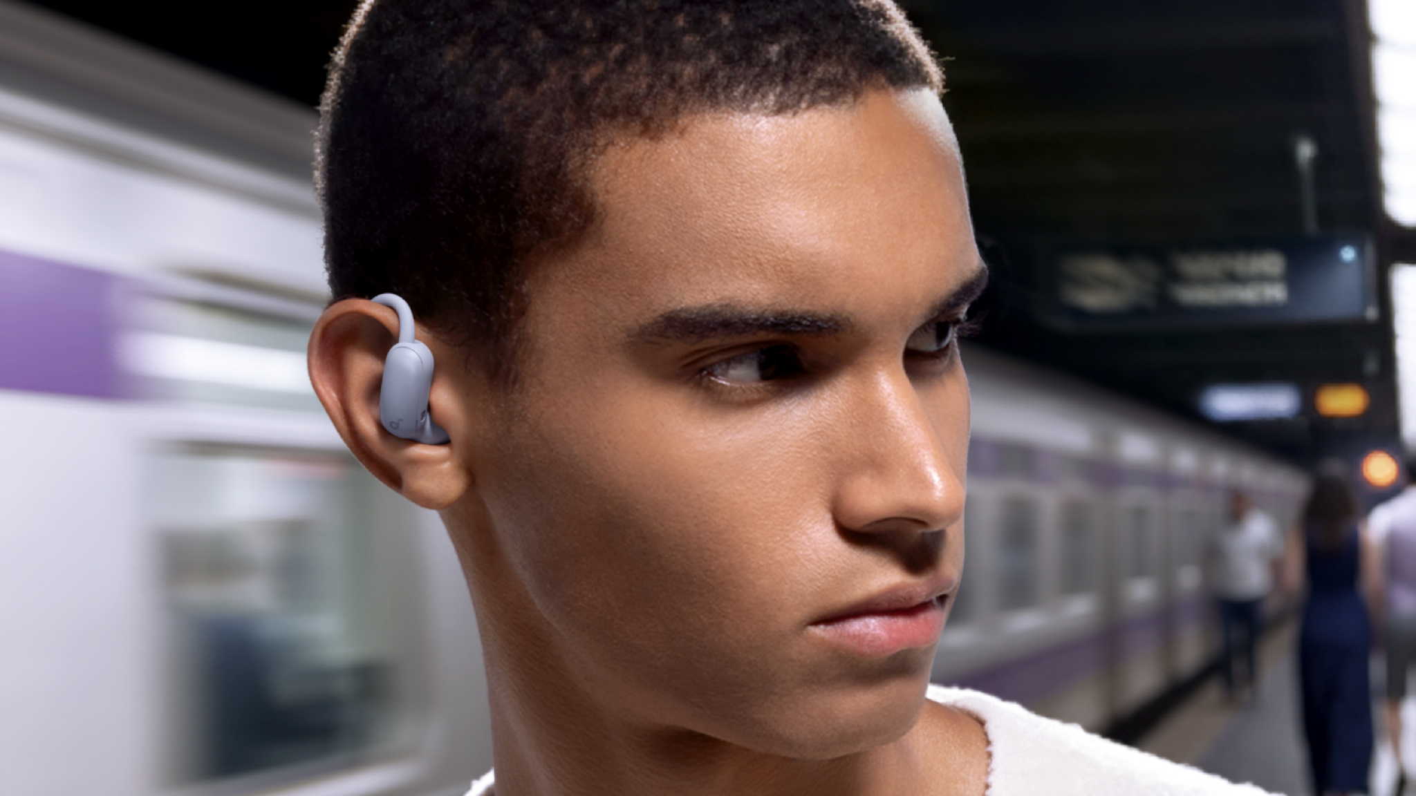 A young man in a subway station wearing Soundcore AeroFit 2 Pro earbuds