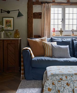 cottage living room with low beamed ceilings and a navy blue couch with striped cushions and a white blue and orange floral skirted ottoman