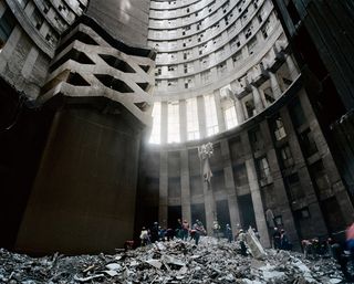 Several people standing on top of a pile of rubbish inside a tall building which has light shining through the windows