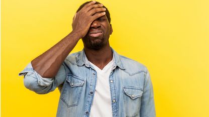 Young man covers his face with one hand in gesture of regret.