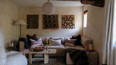 Rustic living room with beams, lime wash walls, tapestries on walls, boucle sectional sofa, woven cushions and lantern pendant light