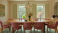 Dining room with cream colored walls and a large wooden oval table in the center with upholstered pink dining chairs